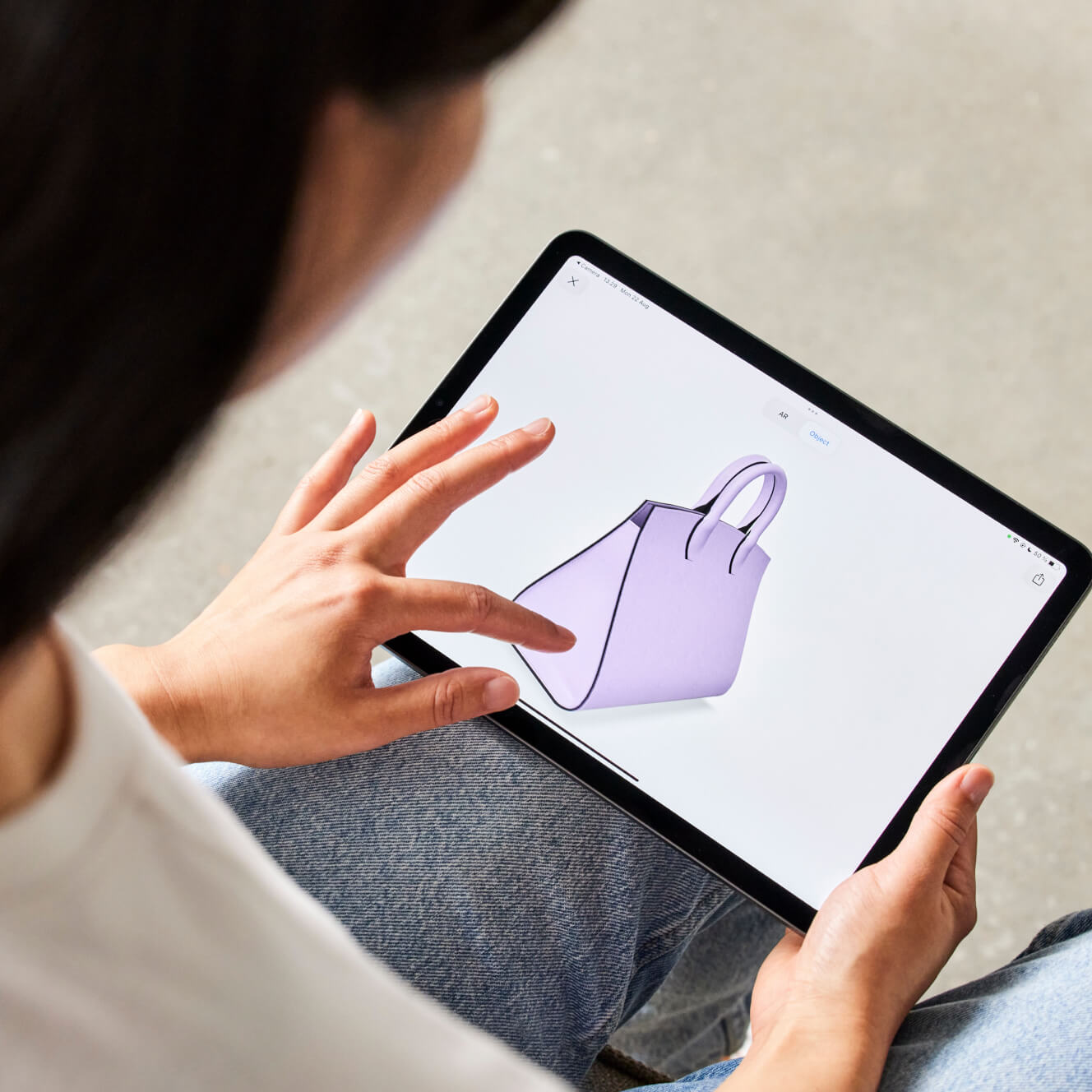 Person interacting with a 3D visualization of a handbag on a tablet device